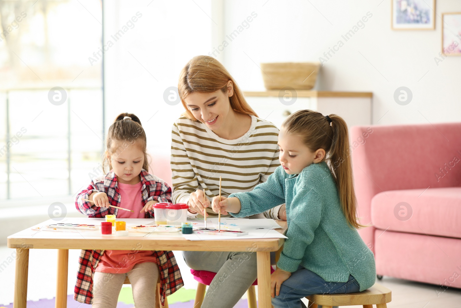 Photo of Mother and daughters painting at table indoors. Playing with children