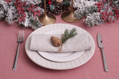 Festive place setting with beautiful dishware, cutlery and cone for Christmas dinner on pink tablecloth