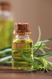 Bottle of essential oil and fresh tarragon leaves on wooden table