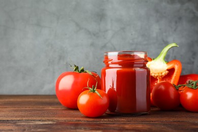 Photo of Jar of tasty ketchup, tomatoes and pepper on wooden table. Space for text