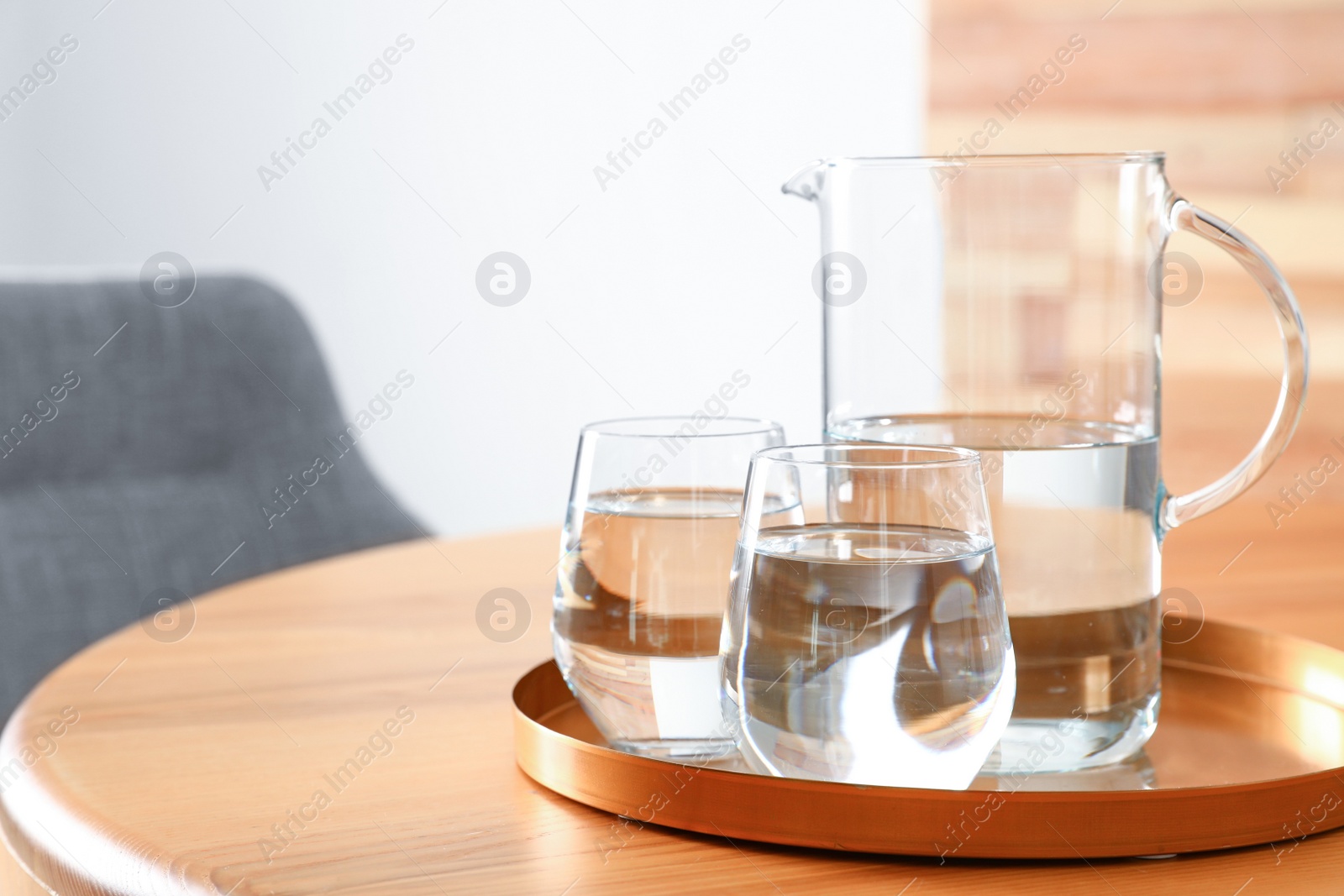 Photo of Tray with jug and glasses of water on wooden table in room, space for text. Refreshing drink