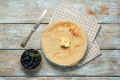 Photo of Stack of delicious crepes with melting butter and fresh berries on wooden table, flat lay