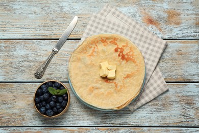 Stack of delicious crepes with melting butter and fresh berries on wooden table, flat lay