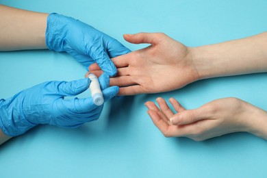 Diabetes. glucose testing. Doctor using lancet pen on light blue background, closeup