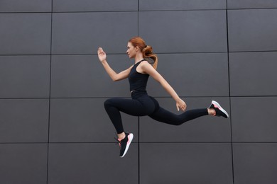 Photo of Beautiful woman in gym clothes jumping near dark grey wall on street