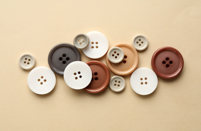 Many colorful sewing buttons on beige background, flat lay