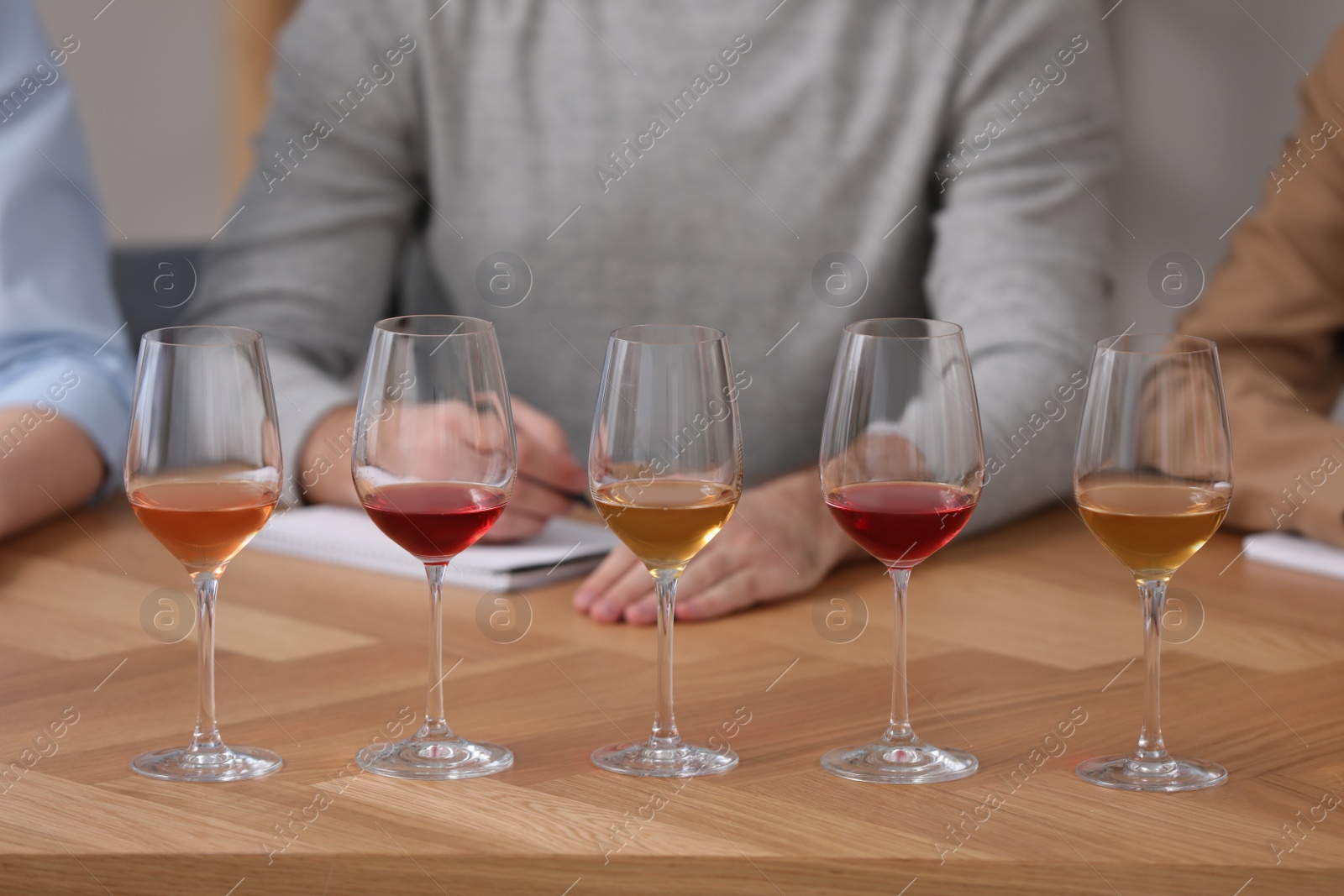 Photo of Different sorts of wine in glasses prepared for tasting and sommeliers at wooden table indoors, closeup