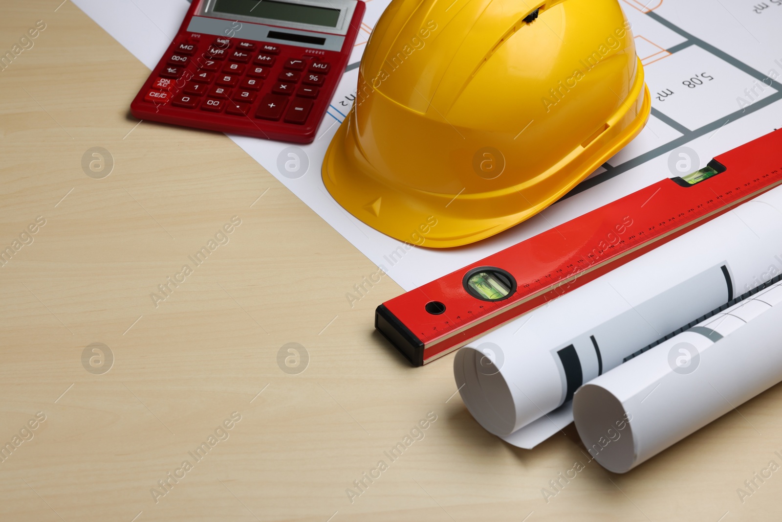 Photo of Construction drawings, safety hat, calculator and bubble level on wooden table. Space for text