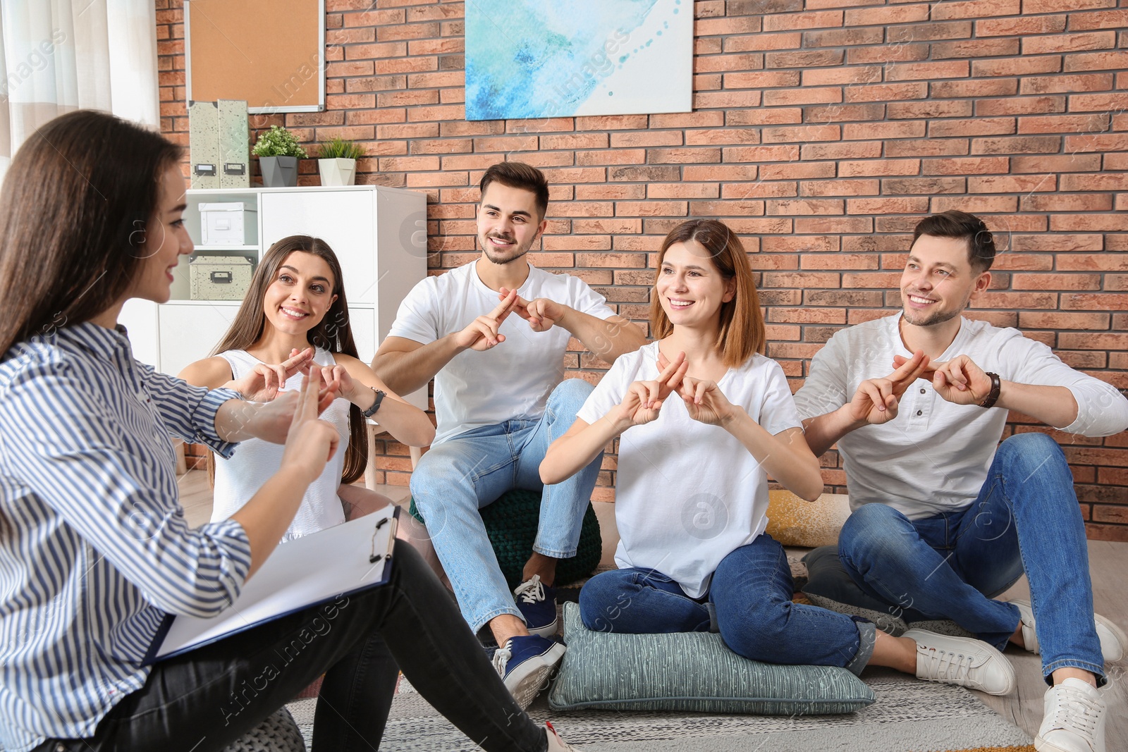 Photo of Group of young people learning sign language with teacher indoors