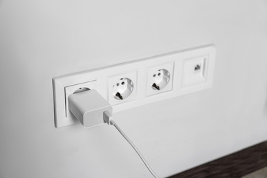 Photo of Charger adapter plugged in power socket indoors, space for text