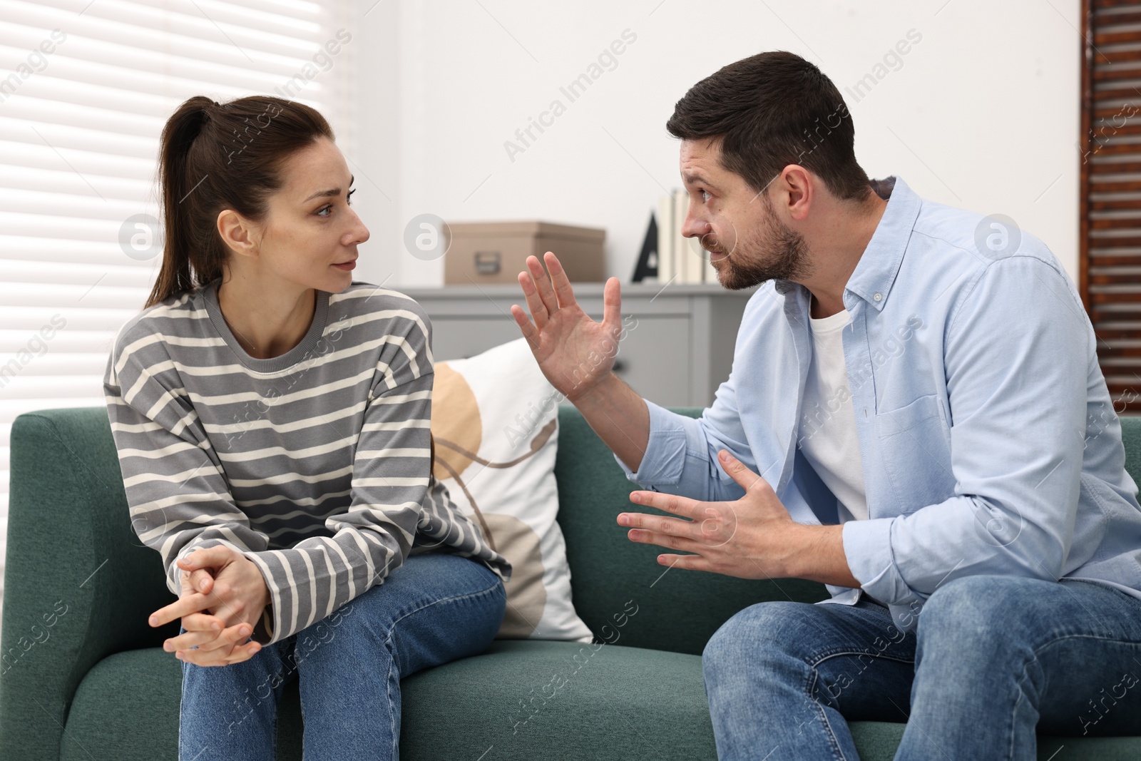 Photo of Emotional couple arguing on sofa indoors. Relationship problems