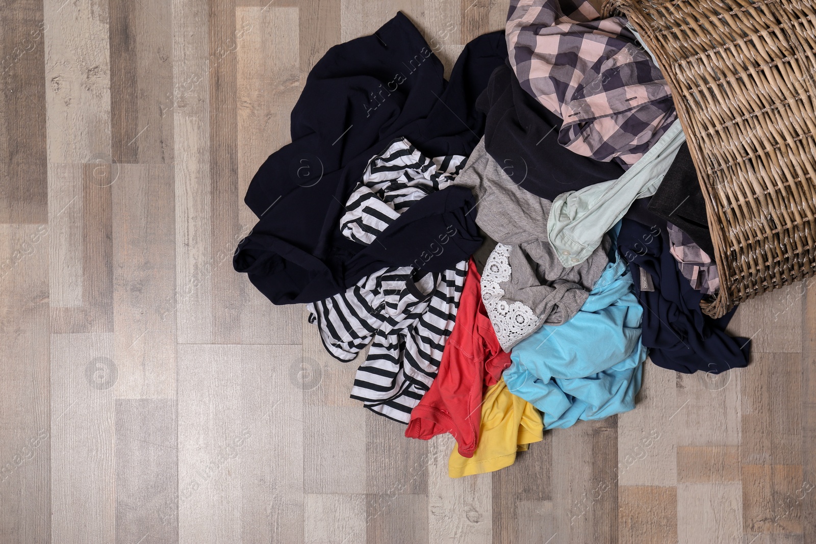 Photo of Dirty clothes scattered from laundry basket on floor, top view. Space for text