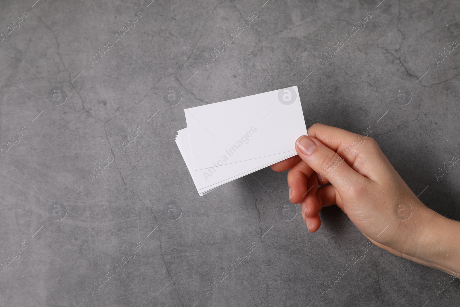 Photo of Woman holding blank cards at grey table, top view. Mockup for design