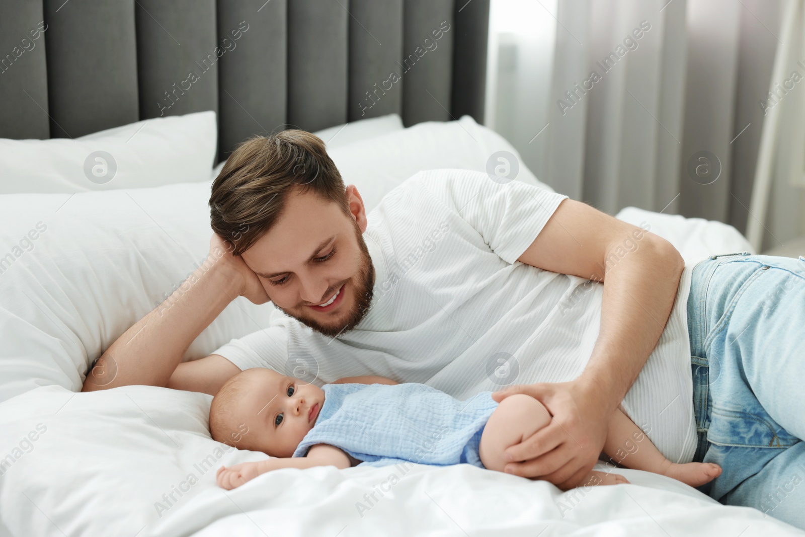 Photo of Father with his cute baby on bed indoors