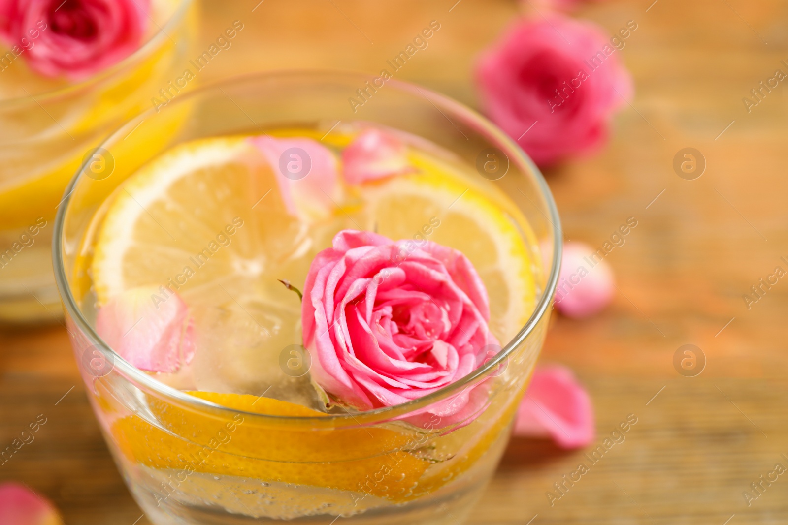 Photo of Tasty refreshing lemon drink with roses on wooden table, closeup