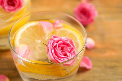 Photo of Tasty refreshing lemon drink with roses on wooden table, closeup