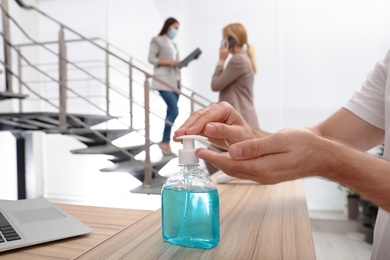 Photo of Man applying hand sanitizer at office reception, closeup