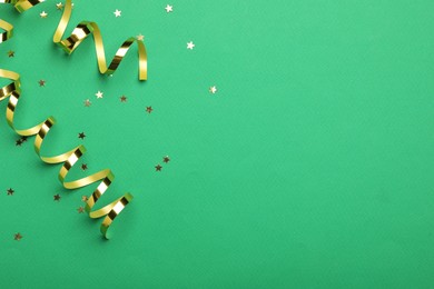 Shiny golden serpentine streamers and confetti on green background, flat lay. Space for text