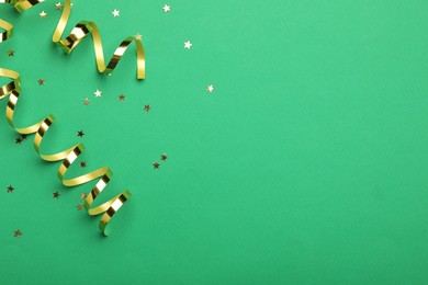 Photo of Shiny golden serpentine streamers and confetti on green background, flat lay. Space for text