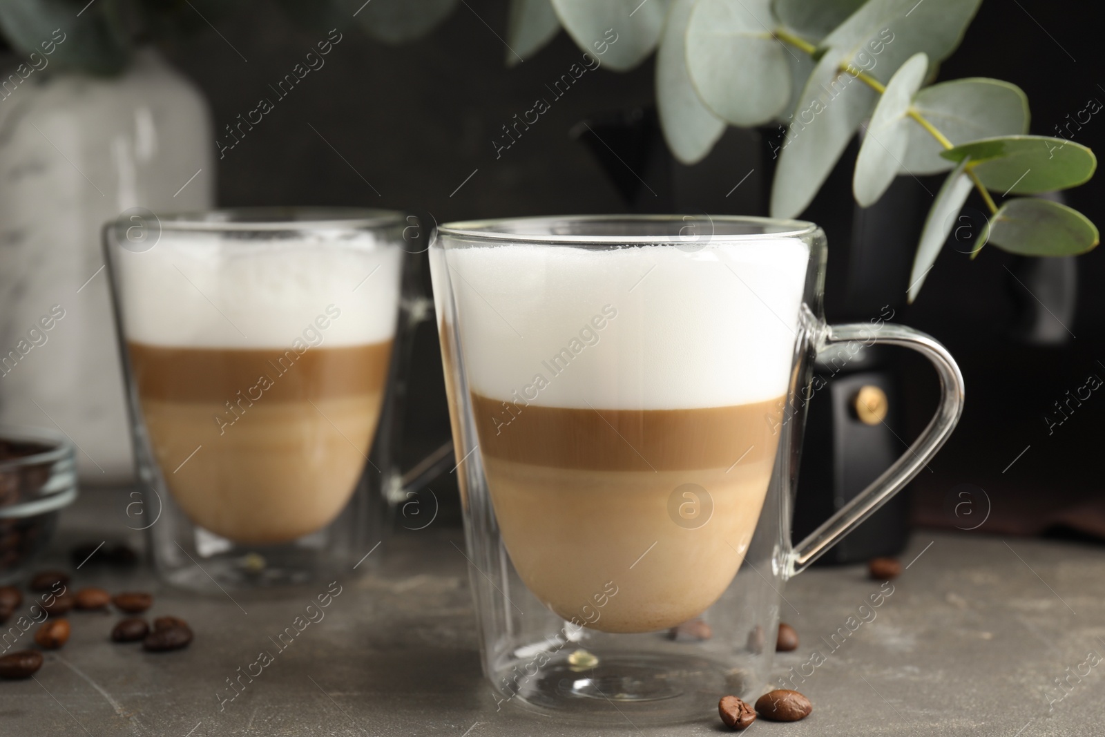 Photo of Glass cups of delicious latte macchiato and scattered coffee beans on grey table