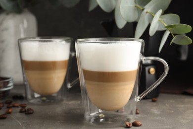 Glass cups of delicious latte macchiato and scattered coffee beans on grey table