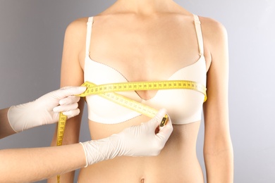 Photo of Doctor measuring size of patient's breast on gray background, closeup. Cosmetic surgery