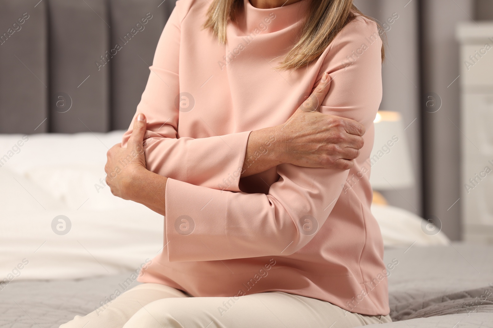 Photo of Mature woman suffering from pain in arms on bed indoors, closeup. Rheumatism symptom