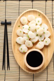 Photo of Raw scallops with green onion, soy sauce and chopsticks on bamboo mat, top view