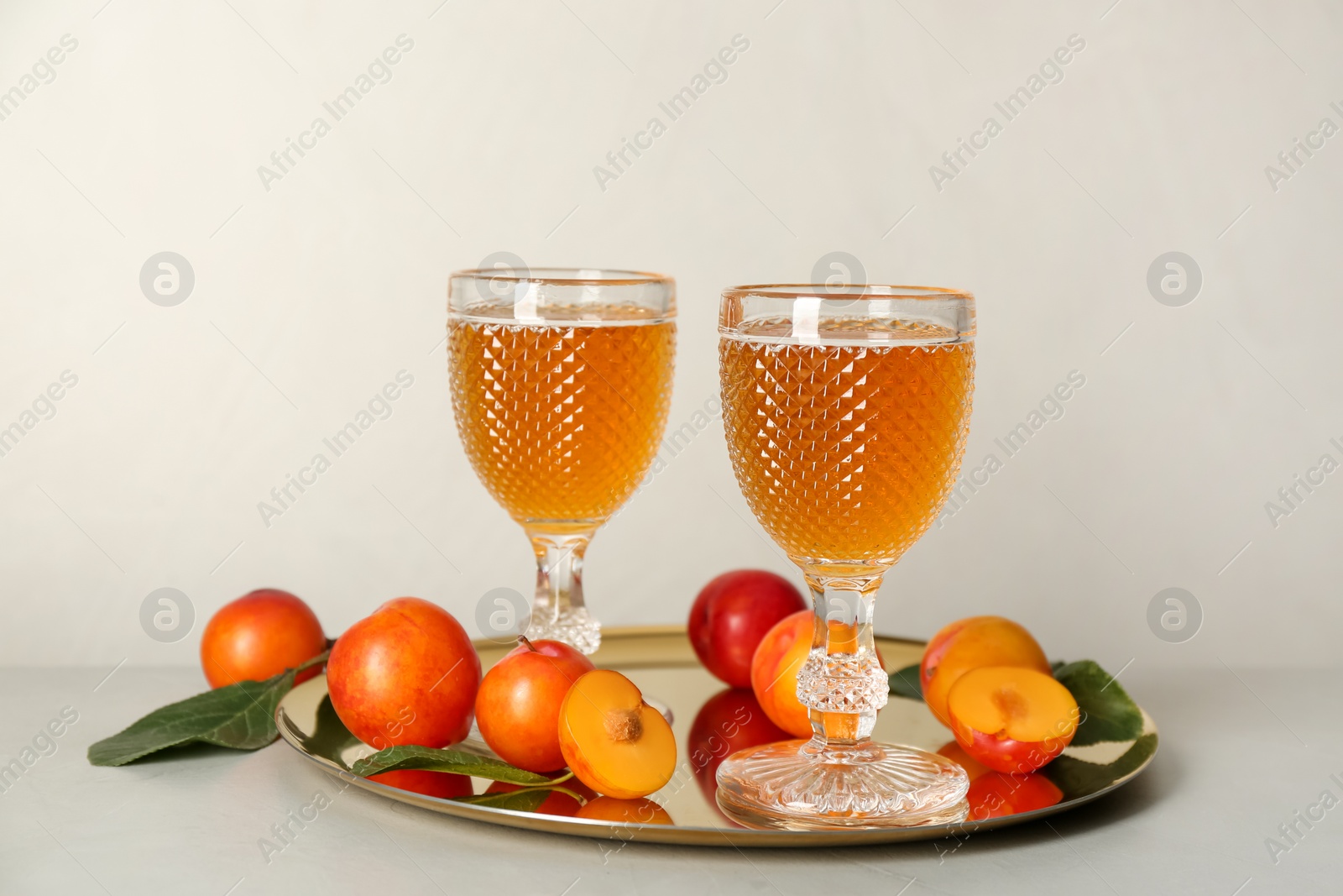 Photo of Delicious plum liquor and ripe fruits on light table. Homemade strong alcoholic beverage