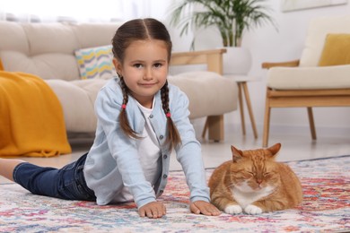 Photo of Little girl and cute ginger cat on carpet at home