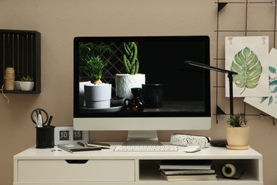 Photo of Stylish workplace with computer on white desk near beige wall. Interior design
