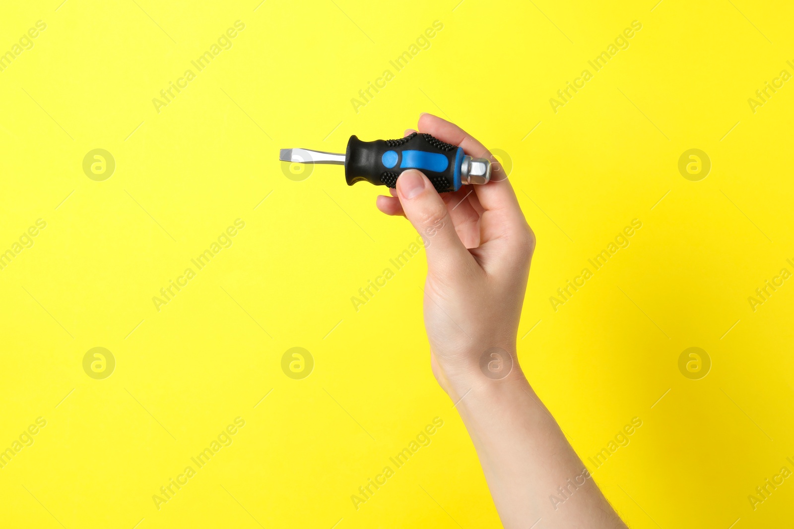 Photo of Woman holding small screwdriver on yellow background, closeup