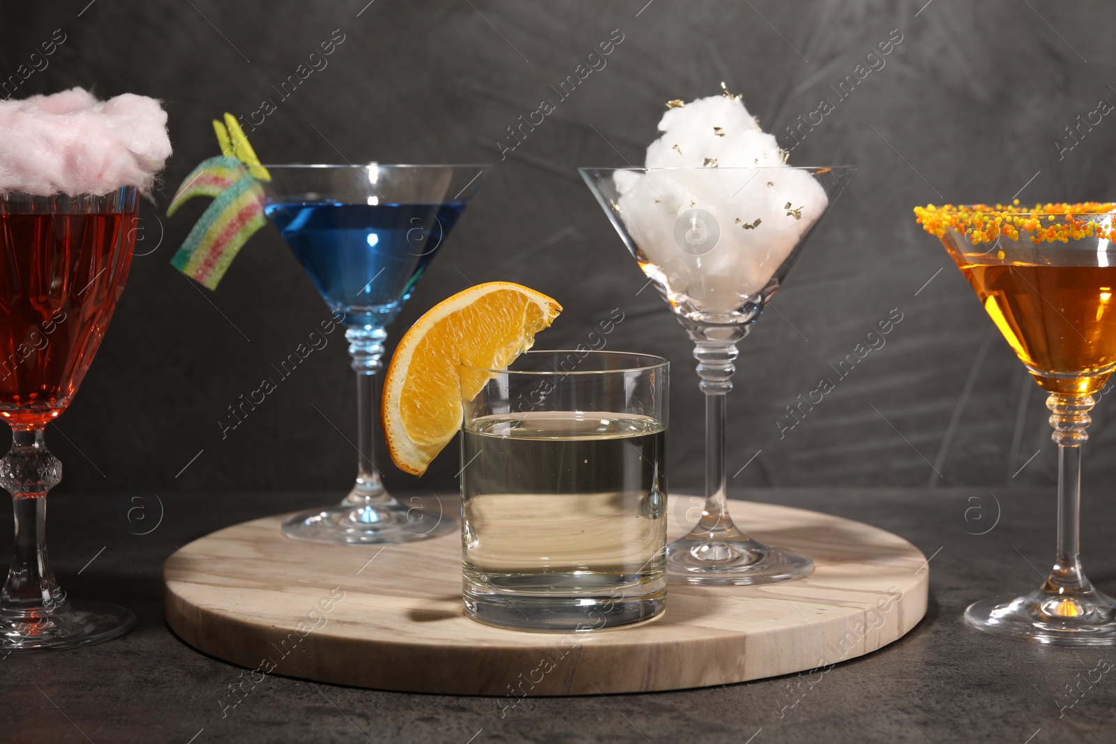 Photo of Tasty cotton candy cocktail and other alcoholic drinks in glasses on gray textured table