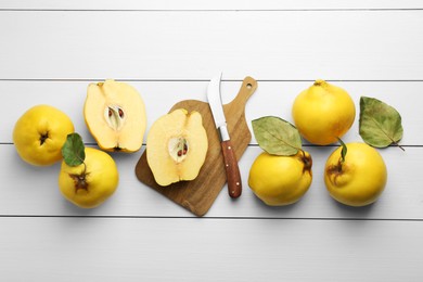 Photo of Tasty ripe quince fruits and knife on white wooden table, flat lay