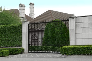Photo of Beautiful stone fence with ornate black metal gates around house and garden