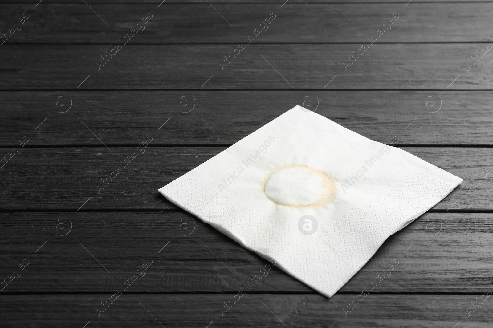 Photo of Paper napkin with coffee stain and space for text on wooden background