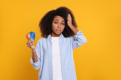 Confused woman with credit cards on orange background. Debt problem