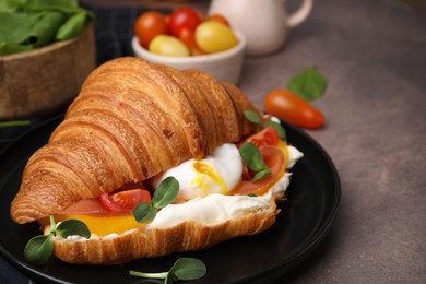 Photo of Tasty croissant with fried egg, tomato and microgreens on brown textured table, closeup