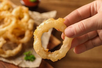 Photo of Woman holding homemade crispy onion ring over table, closeup