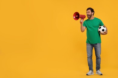 Photo of Emotional sports fan with soccer ball and megaphone on orange background, space for text