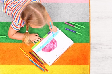 Photo of Little left-handed girl drawing on floor in room, above view