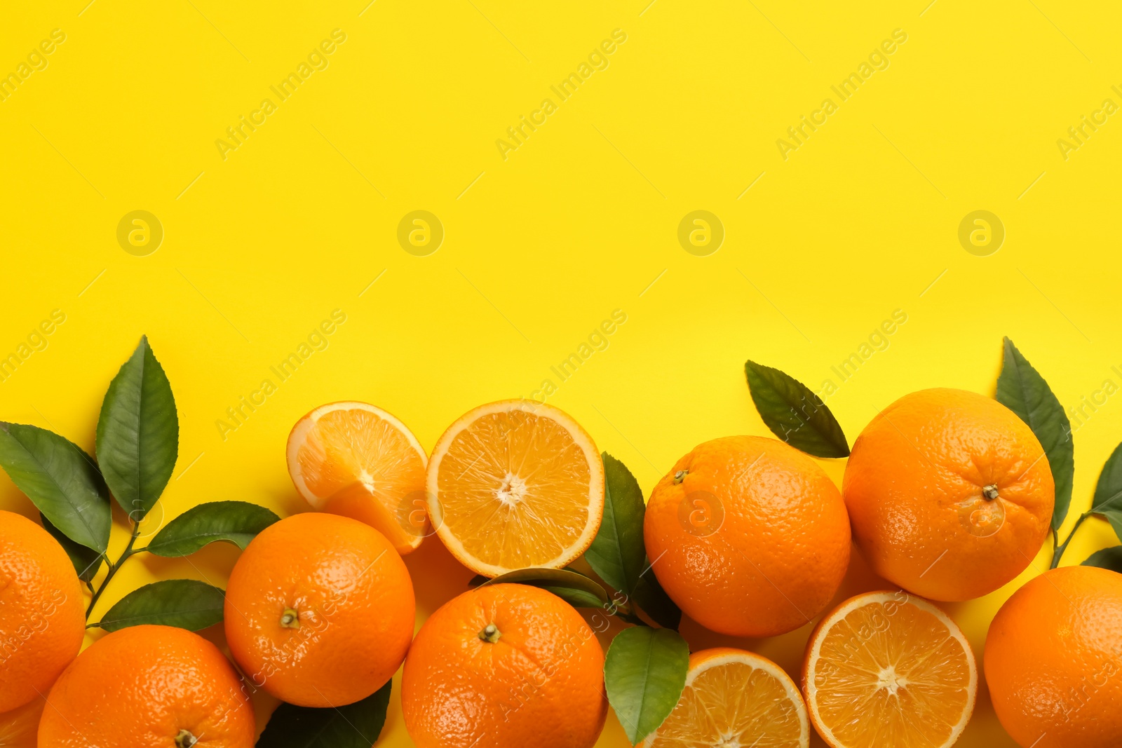 Photo of Fresh ripe oranges with green leaves on yellow background, top view. Space for text