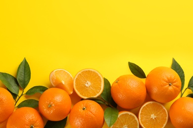 Photo of Fresh ripe oranges with green leaves on yellow background, top view. Space for text