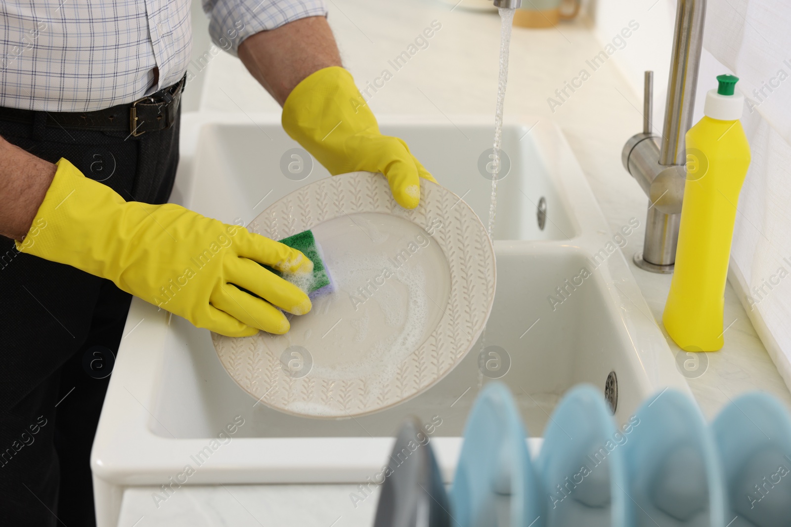 Photo of Man in protective gloves washing plate above sink in kitchen, closeup