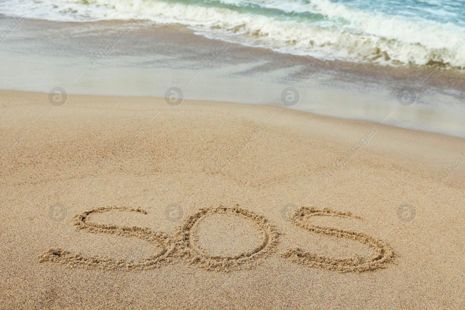 Photo of Message SOS drawn on sand near sea