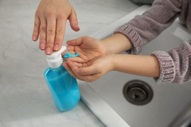 Photo of Mother and daughter washing hands with liquid soap together at home, closeup