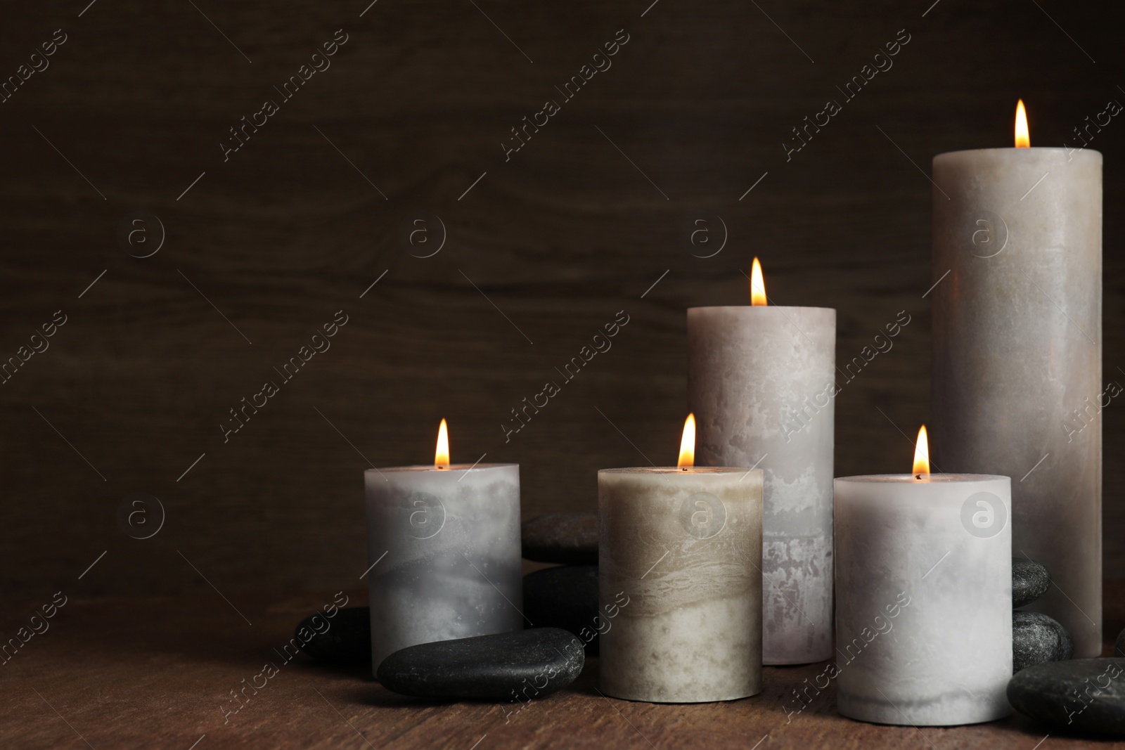 Photo of Burning candles and spa stones on wooden table, space for text