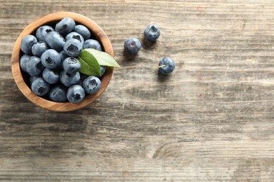 Photo of Bowl of fresh tasty blueberries on wooden table, flat lay. Space for text
