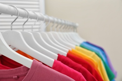 Photo of Rack with bright clothes in room. Rainbow colors