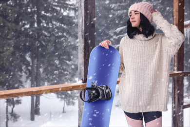 Young woman with snowboard wearing winter sport clothes outdoors